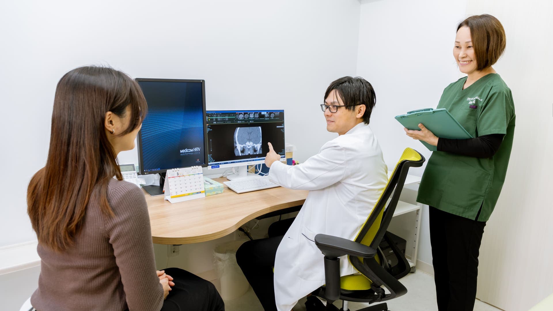 提携医療機関の診察室。医師が画像診断モニターを見せながらお客様に説明し、施術スタッフが横で控えている